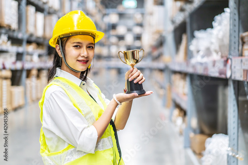 Fotografie Happy woman warehouse worker holding a trophy after being selected as an outstan