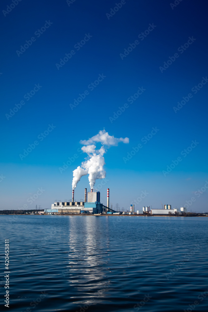 View of the coal-fired power plant located by the lake. Patnow, Polamd. Made on a sunny day. Deep blue sky.