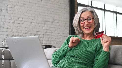 Well-dressed gray haired woman on retirement paid for trip around the world, made dream come true, managing her budget using special app, laughs with happiness, easy and fast payment with credit card photo