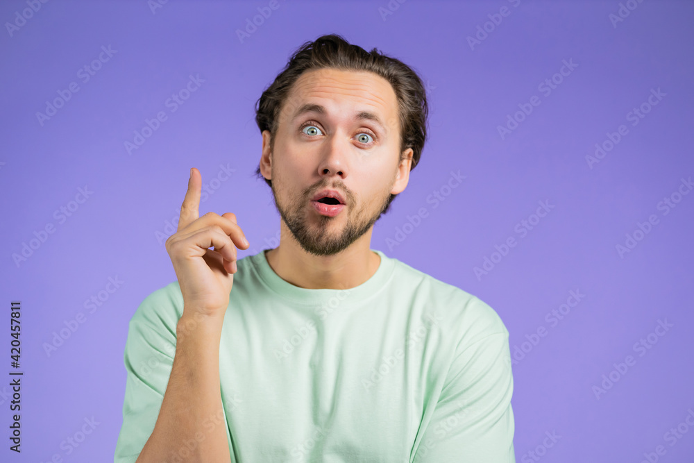 Surprised guy showing eureka gesture. Portrait of young man having idea moment pointing finger up on violet studio background. Surprised guy showing eureka gesture. Portrait of young man having idea moment pointing finger up on violet studio background.
