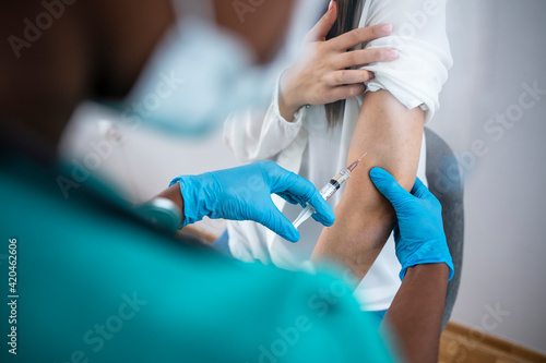 Vaccination, immunization, disease prevention concept. Woman in medical face mask getting Covid-19 or flu vaccine at the hospital. Professional nurse or doctor giving antiviral injection to patient