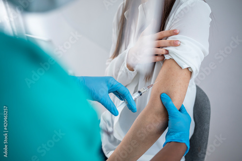 Professional doctor or nurse giving flu or COVID-19 injection to patient. Woman in medical face mask getting antiviral vaccine at hospital or health center during vaccination and immunization campaign