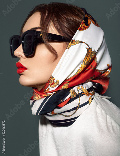 isolated portrait of a woman in head scarf look to the side in black sunglasses and red lips
