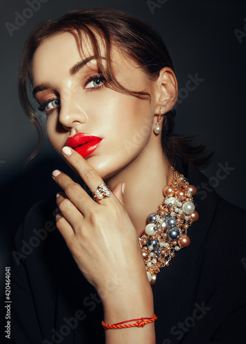 caucasian Woman with red lips in dark suit shows beads necklace and ring