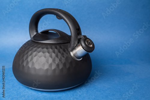 black metal teapot with whistle and plastic handle on blue background