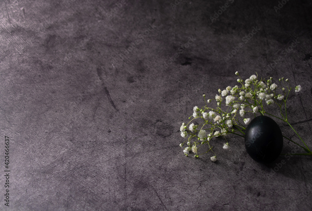 One black Easter egg and wildflowers on a gray surface. Horizontal background for Easter greetings with space for text. One black Easter egg and wildflowers on a gray surface. Horizontal background for Easter greetings with space for text.