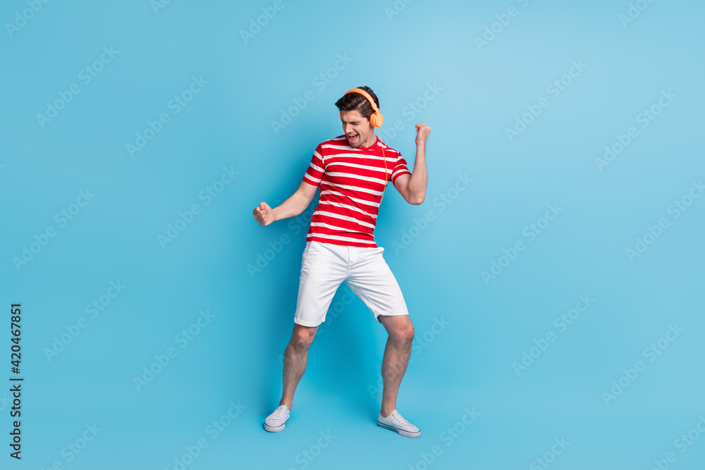 Full length body size photo of guy dancing singing in orange headphones wearing stylish outfit isolated on vivid blue color background Full length body size photo of guy dancing singing in orange headphones wearing stylish outfit isolated on vivid blue color background