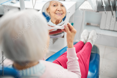 Aging female checking her teeth in mirror from dental chair