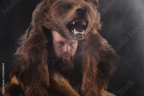 Bild auf Leinwand Low key portrait of a bearded war shaman in bearskin with an ancient ax in his hands
