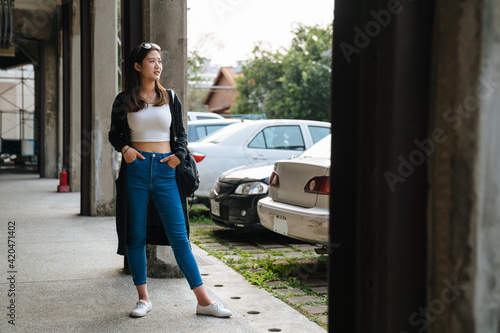 young stylish sexy girl in sunglasse with hands in jeans pockets standing outdoor urban parking lot. hipster casual style female looking aside. full length beautiful lady patiently waiting in walkway
