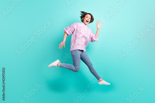 Full length photo of shiny excited young lady dressed purple pullover jumping waving arm isolated teal color background