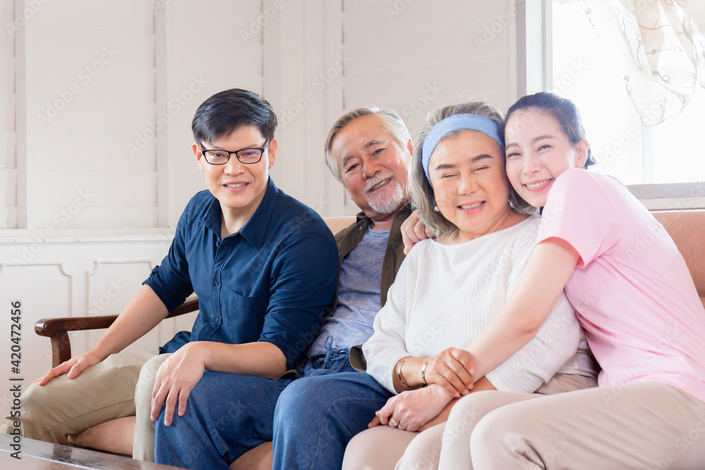 Cheerful Asian family in living room, Senior father mother and middle aged son and daughter sitting on sofa looking at camera, Happiness family concepts Cheerful Asian family in living room, Senior father mother and middle aged son and daughter sitting on sofa looking at camera, Happiness family concepts