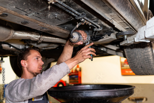 Car mechanic replacing fuel filter, in under the background car on a lift in a car workshop. Repair and replacement of car parts in a service center. © Marko