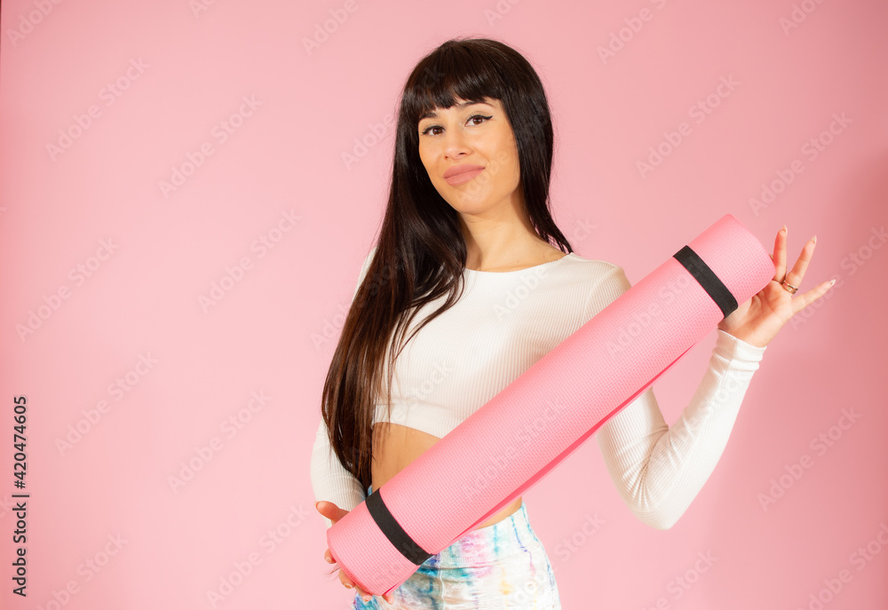 Happy young woman holding a yoga mat isolated over pink background. Happy young woman holding a yoga mat isolated over pink background.