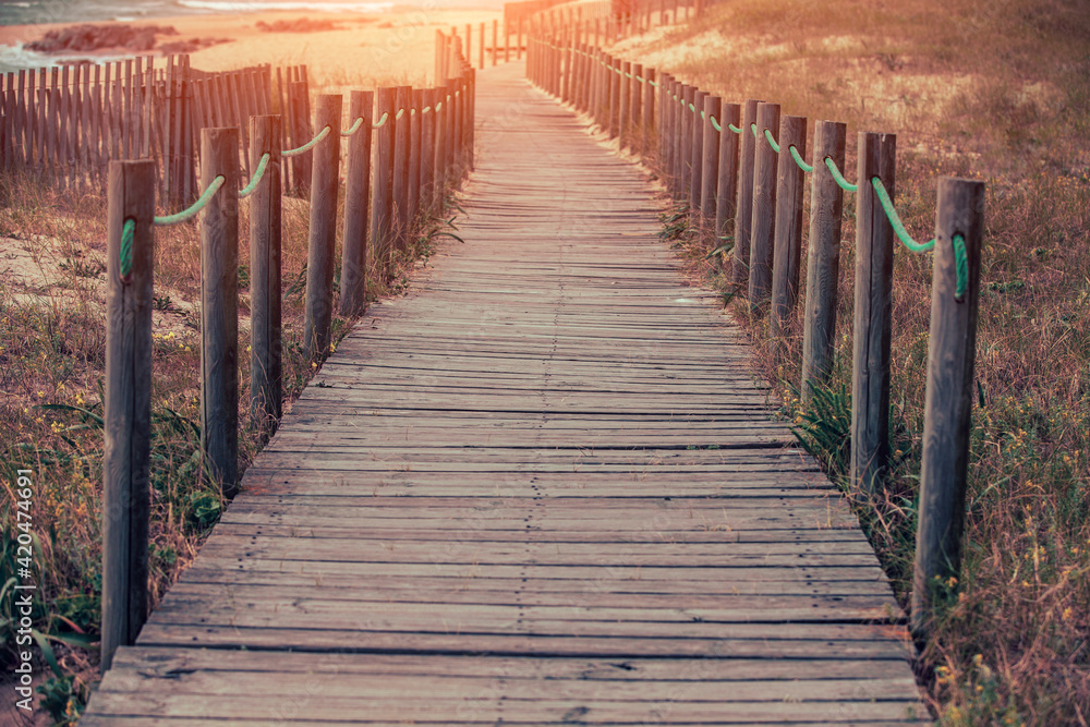 Obraz premium Wooden walkway on the sandy seashore in the magical light of the sunset. Beautiful seascape in the evening. Porto, Portugal