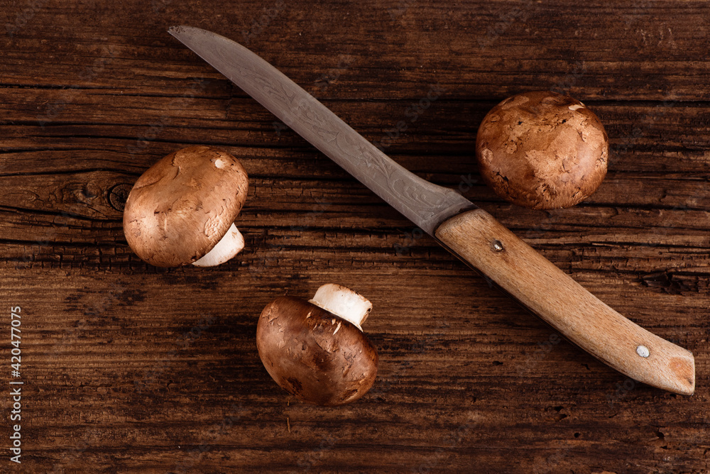 Cremini mushrooms and old kitchen knife on textured wood background. Three baby portobello. Closeup.