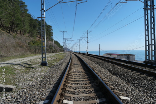 Railroad rails with concrete sleepers and electric wires. There are mountain and sea around. Photographed on a sunny day