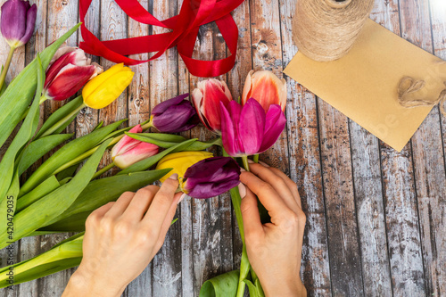 Close-up of female hands make a bouquet of tulips in floral shop. Floral design studio, making decorations and arrangements. Flowers delivery, creating order, spring gift concept