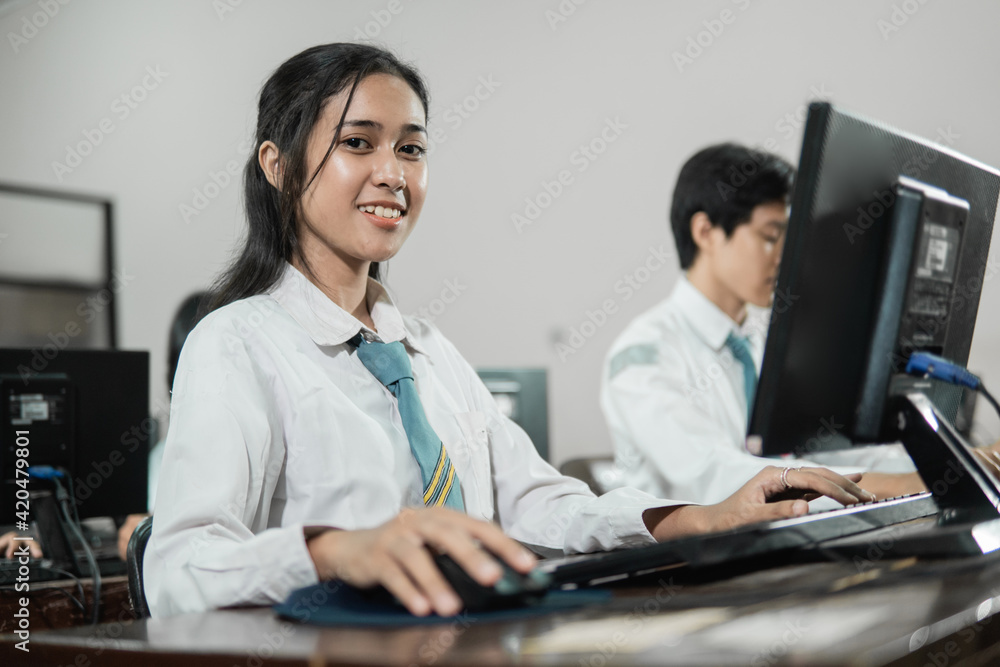 female high school students smile looking at the camera while using a computer PC with their friends studying in a computer practice room at school female high school students smile looking at the camera while using a computer PC with their friends studying in a computer practice room at school