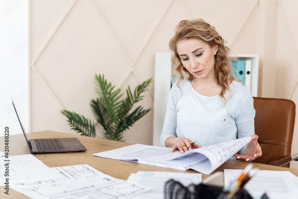 Woman sitting in office, looking at blueprint Woman sitting in office, looking at blueprint