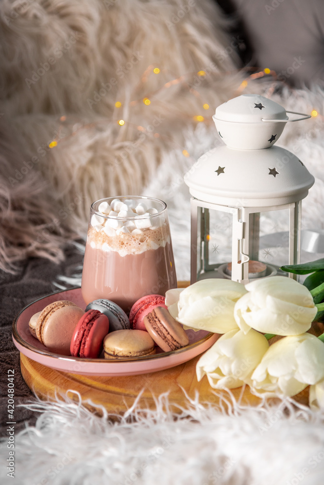 A glass of hot cocoa with marshmallows, macaroni cakes and white tulips on a tray in bed. Cozy spring home concept, vertical photo A glass of hot cocoa with marshmallows, macaroni cakes and white tulips on a tray in bed. Cozy spring home concept, vertical photo
