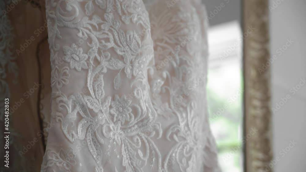 Beautiful details of a wedding dress up close as it is hanging in a mirror in a white well lit and clean room. Beautiful details of a wedding dress up close as it is hanging in a mirror in a white well lit and clean room.