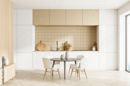 Modern kitchen interior, dining area with panoramic windows. Furnished by table and chairs for eating, wooden sideboard. Parquet floor.