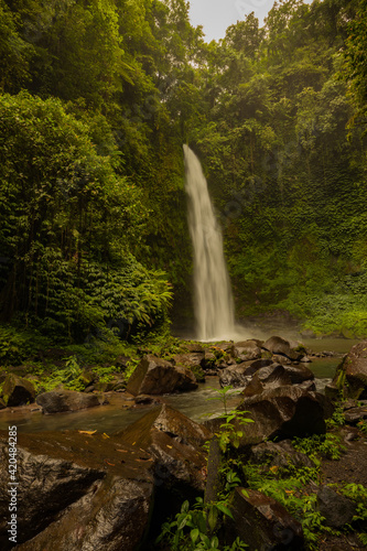 Waterfall landscape. Beautiful hidden waterfall in tropical rainforest. Foreground with big stones. Slow shutter speed, motion photography. Travel and adventure. Nung Nung waterfall, Bali