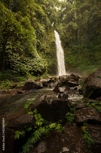 Waterfall landscape. Beautiful hidden waterfall in tropical rainforest. Foreground with big stones. Slow shutter speed, motion photography. Travel and adventure. Nung Nung waterfall, Bali