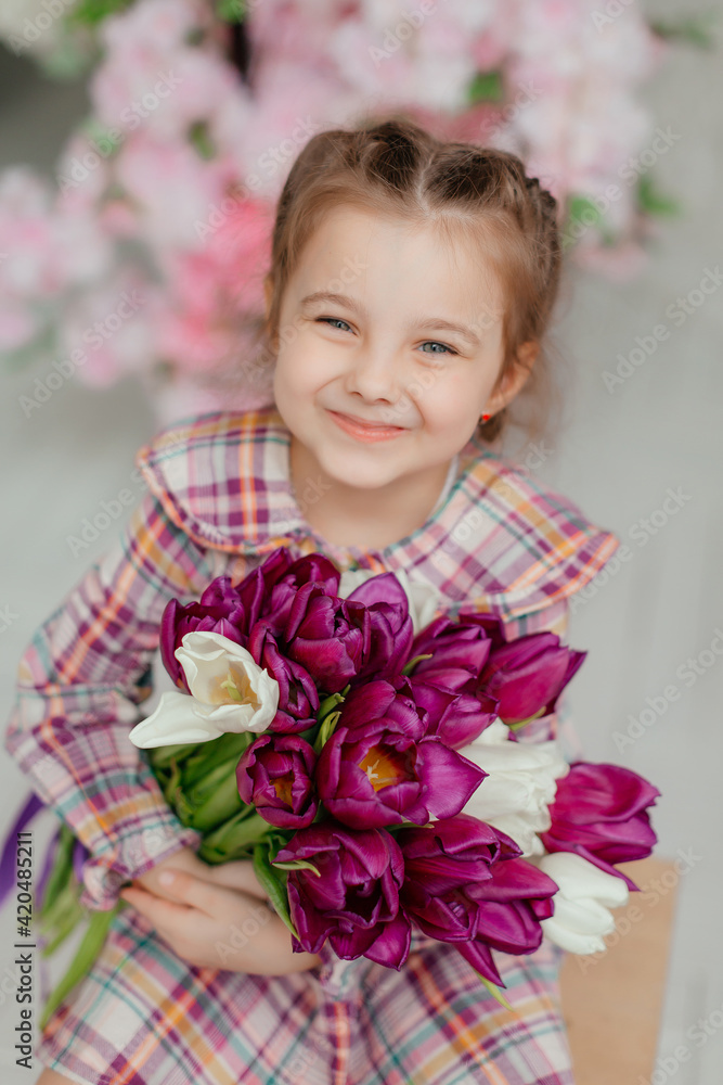 Cute adorable little girl in a dress holding a bouquet of tulip flowers, in a bright photo studio. Cute adorable little girl in a dress holding a bouquet of tulip flowers, in a bright photo studio.