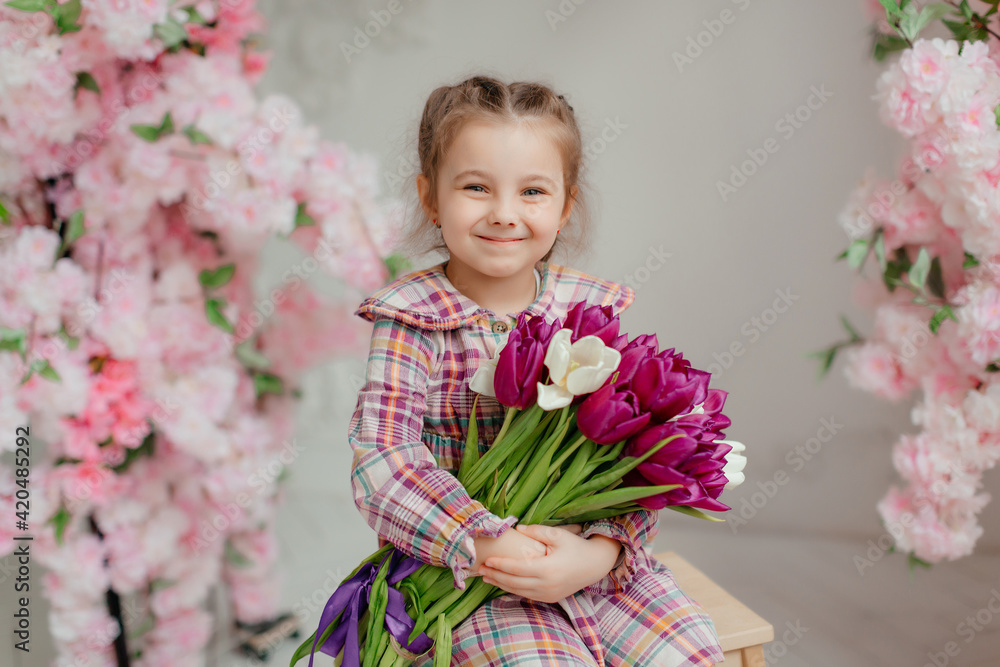 Cute adorable little girl in a dress holding a bouquet of tulip flowers, in a bright photo studio. Cute adorable little girl in a dress holding a bouquet of tulip flowers, in a bright photo studio.