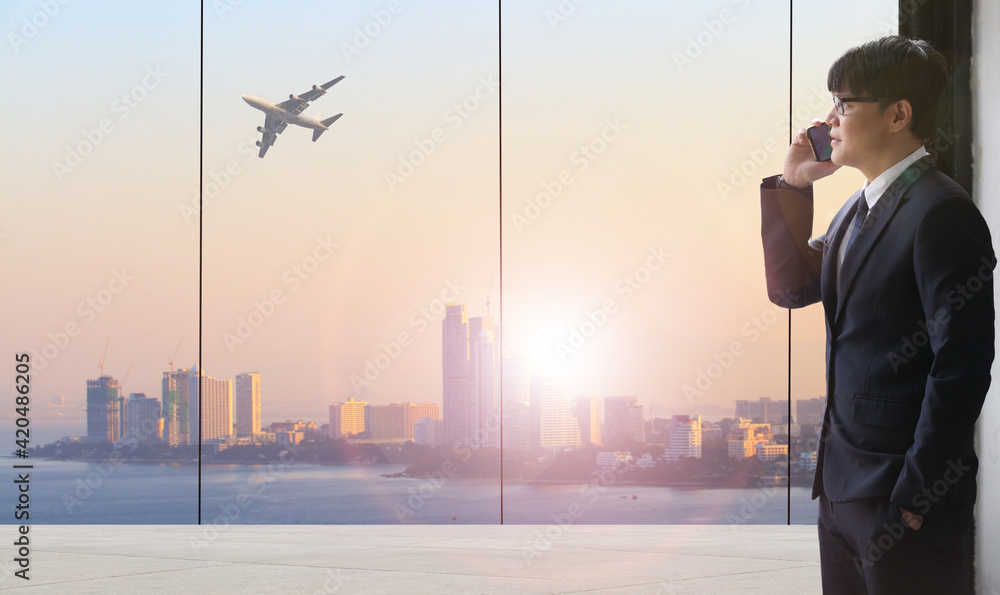 Full length rear view of a young stylish businessman standing at the large windows of a high office, looking at the view of a harbor below,logistics or transportation concept Full length rear view of a young stylish businessman standing at the large windows of a high office, looking at the view of a harbor below,logistics or transportation concept