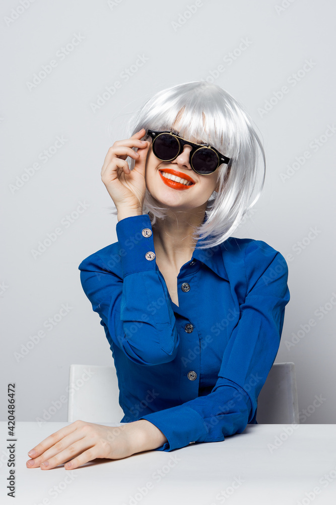 cheerful glamorous Woman in a White wig sits at the table with emotion blue shirt