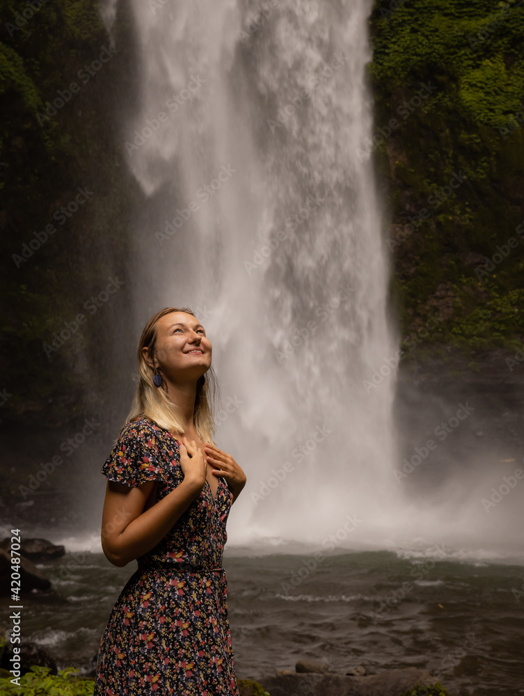 Happy woman smiling and enjoying waterfall landscape. Nature and environment concept. Travel lifestyle. Woman wearing dress. Copy space. Nung Nung waterfall in Bali Happy woman smiling and enjoying waterfall landscape. Nature and environment concept. Travel lifestyle. Woman wearing dress. Copy space. Nung Nung waterfall in Bali