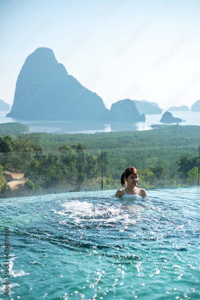 Happy woman in white swimsuit swimming in luxury pool hotel against Phang Nga bay background, Tourist relaxing at Samet Nang She, near Phuket in Southern Thailand. travel, trip and summer vacation