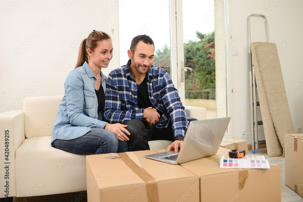 Young happy couple moving in new house and calling friends and family with laptop computer in their brand new apartment Young happy couple moving in new house and calling friends and family with laptop computer in their brand new apartment