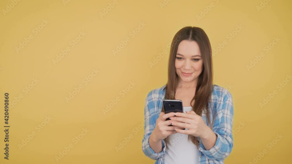 Calm young woman student on yellow background looking looks at smartphone Calm young woman student on yellow background looking looks at smartphone