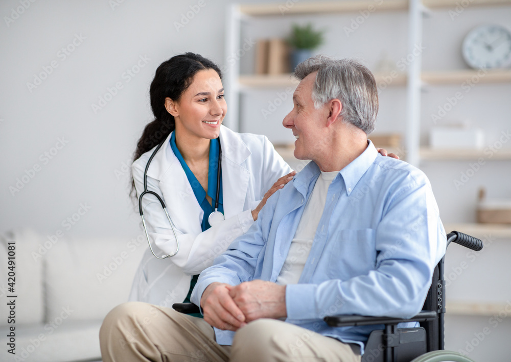 Fototapeta premium Impaired senior man in wheelchair and young nurse taking care of him at home