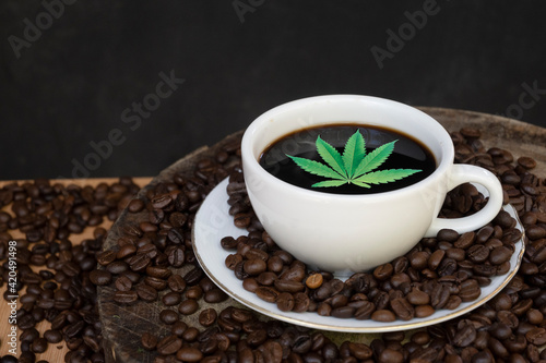 Coffee cups, coffee beans and cannabis leaves on black background The concept of drinking coffee with herbal ingredients, cannabis leaves, is legally licensed by law.