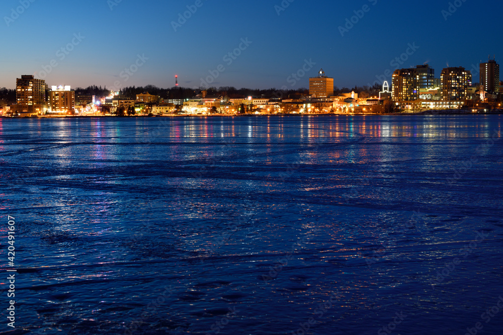 Downtown city lights of Barrie Canada reflected on ice of frozen Kempenfelt Bay Lake Simcoe at twilight on a cold winter night