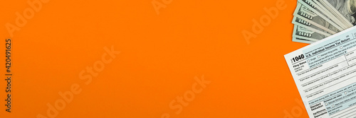 US individual Income Tax Form 1040 with dollar bills on the desktop, orange background with copy space