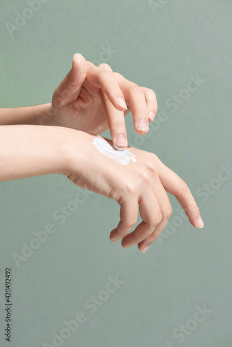 Woman applies cream on her hands isolated on green background