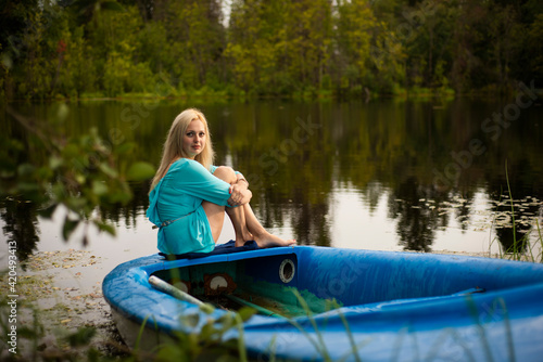 blonde girl sitting on a blue boat by the water, selective focus