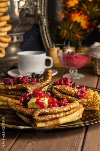 Still life with traditional Ukrainian and Russian pancakes for the Maslenitsa holiday with butter and berries on a black tray