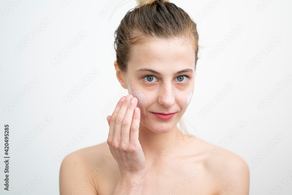 Happy Young Woman Applying Cream on Her Face, Studio Shot on White Background