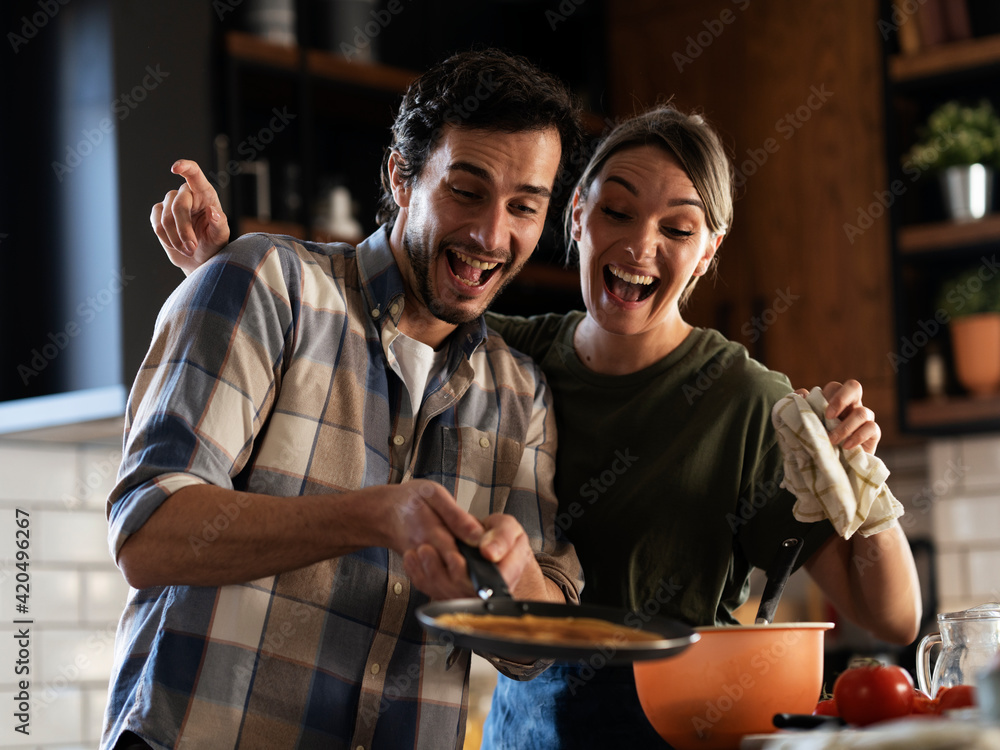 Boyfriend and girlfriend making pancakes at home. Young couple having fun in the kitchen Boyfriend and girlfriend making pancakes at home. Young couple having fun in the kitchen
