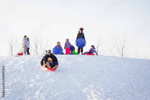 Cute child happily riding down a hill on a toboggan sled with his dad. Interracial family