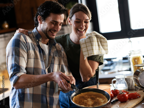 Boyfriend and girlfriend making pancakes at home. Young couple having fun in the kitchen