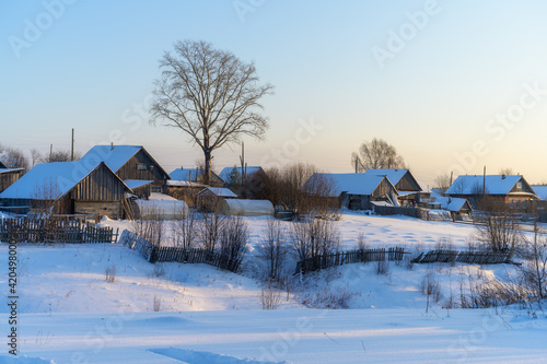 View of the Ural (Russia) village - the Russian hinterland in winter. Mountainous area with tall trees. Traditional style wooden houses with vegetable gardens, sheds and greenhouses in the snow