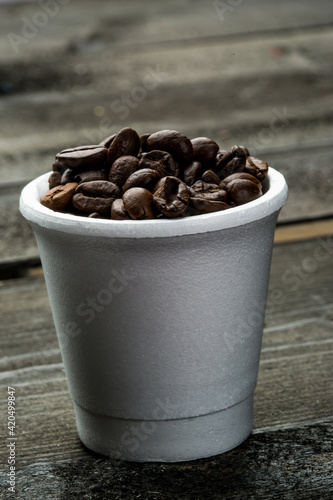 Chicchi di caffe dentro una tazzina, isolati su un tavolo di legno photo